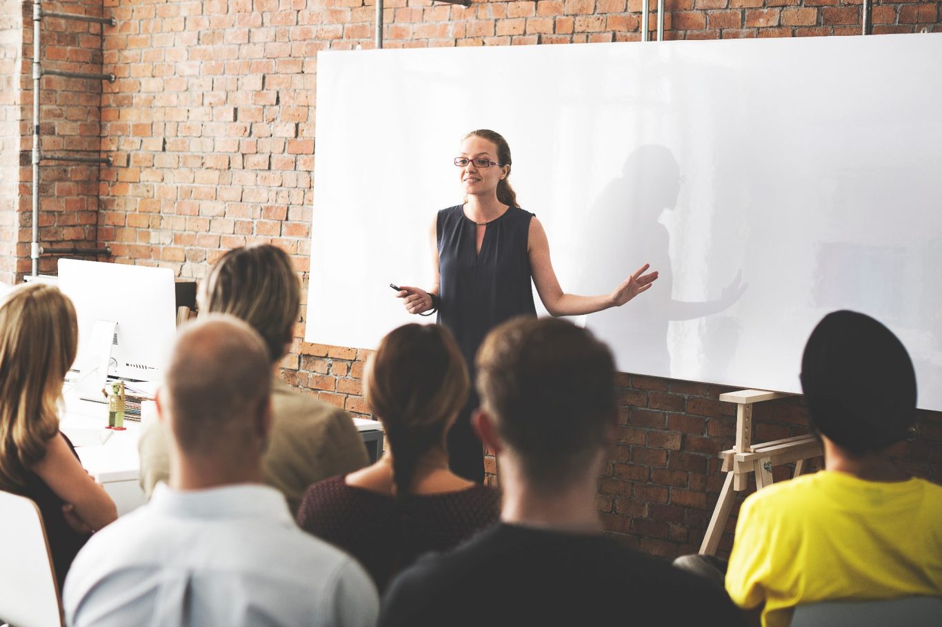 Erfahrung zählt Lehrerin präsentiert vor einer Gruppe, Whiteboard im Hintergrund, entspannte Atmosphäre.